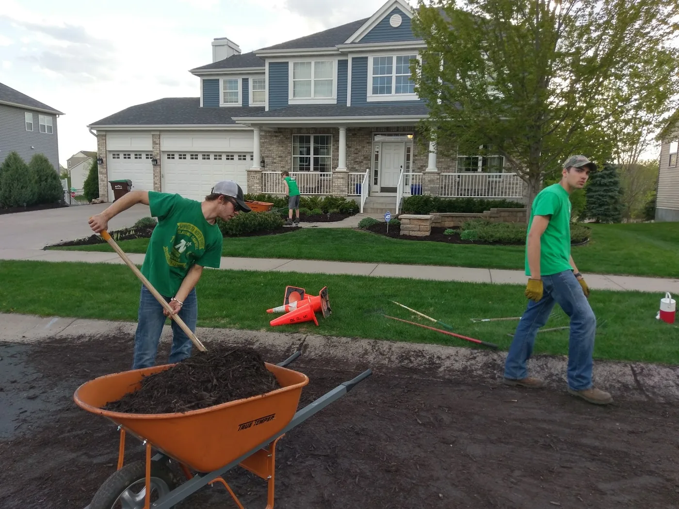 Two West Metro Lawn & Snow crew members spreading mulch and edging landscape beds along a driveway